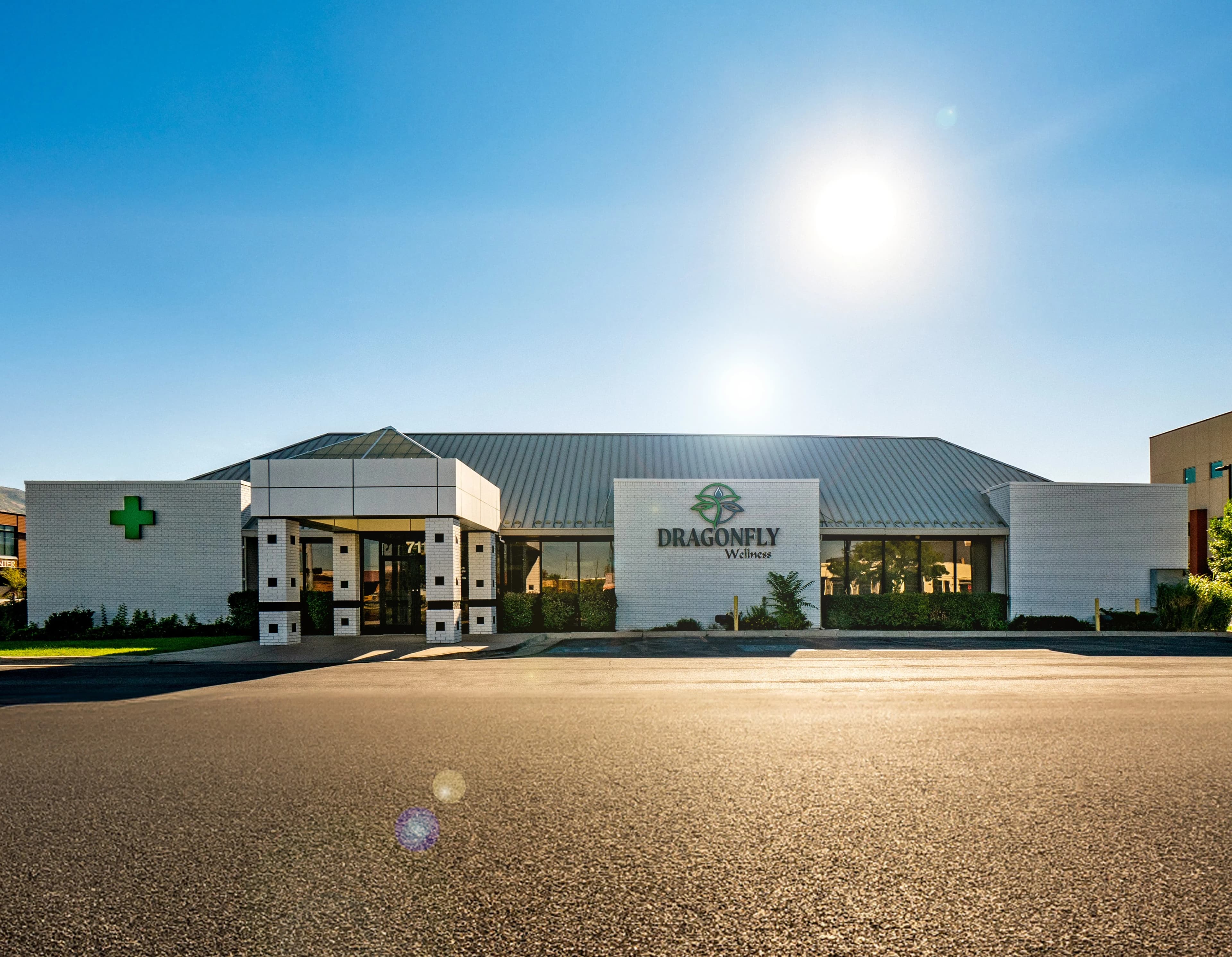 Front view of cannabis pharmacy building in SLC with green cross sign and Dragonfly Wellness logo